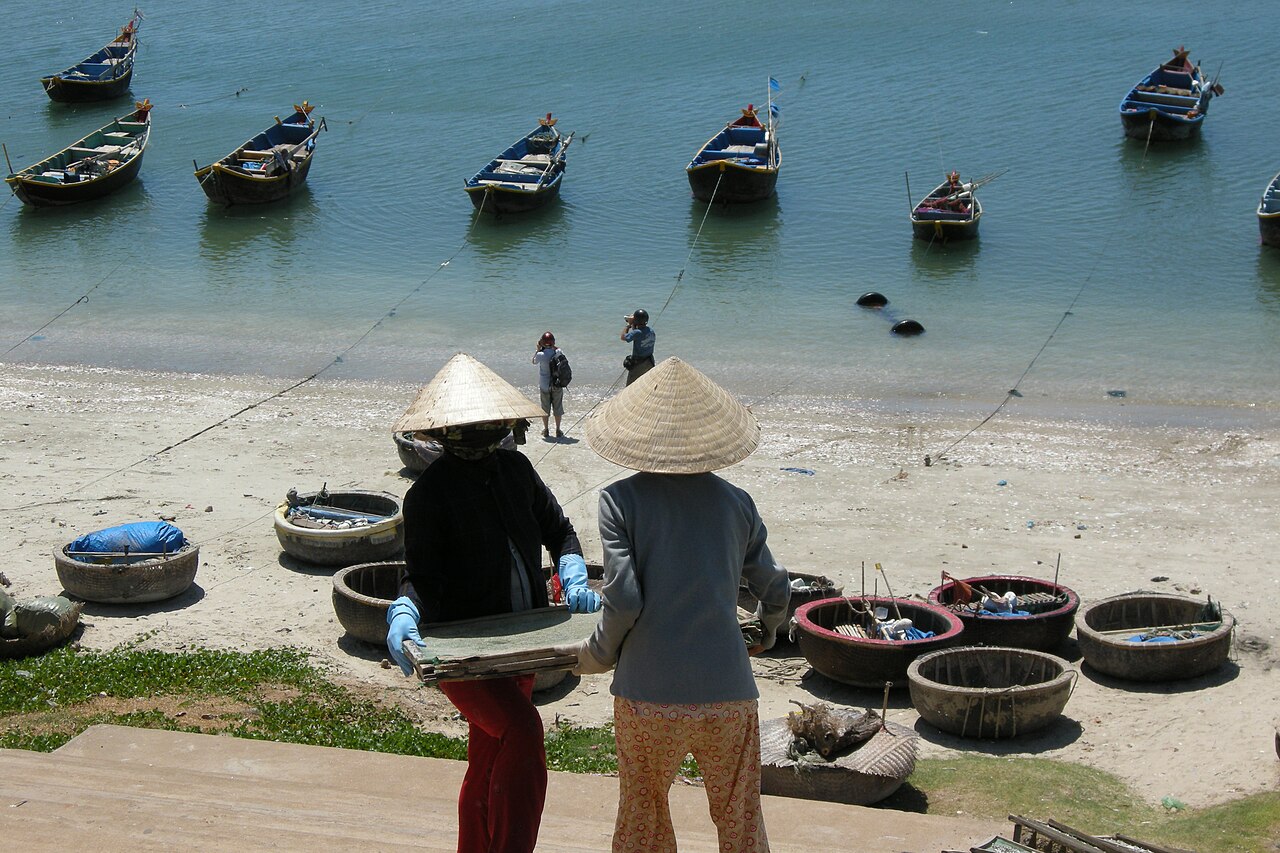 Người dân làm việc bên bờ làng chài Mũi Né, phía sau là thuyền thúng